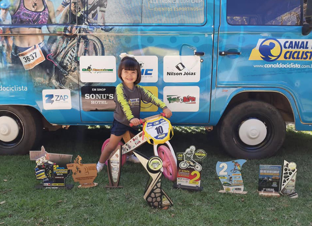 Monica Akemi e Daniel Pianovski, do Canal do Ciclista, com a Biciquetinha e troféus de competições de BMX no Mato Grosso